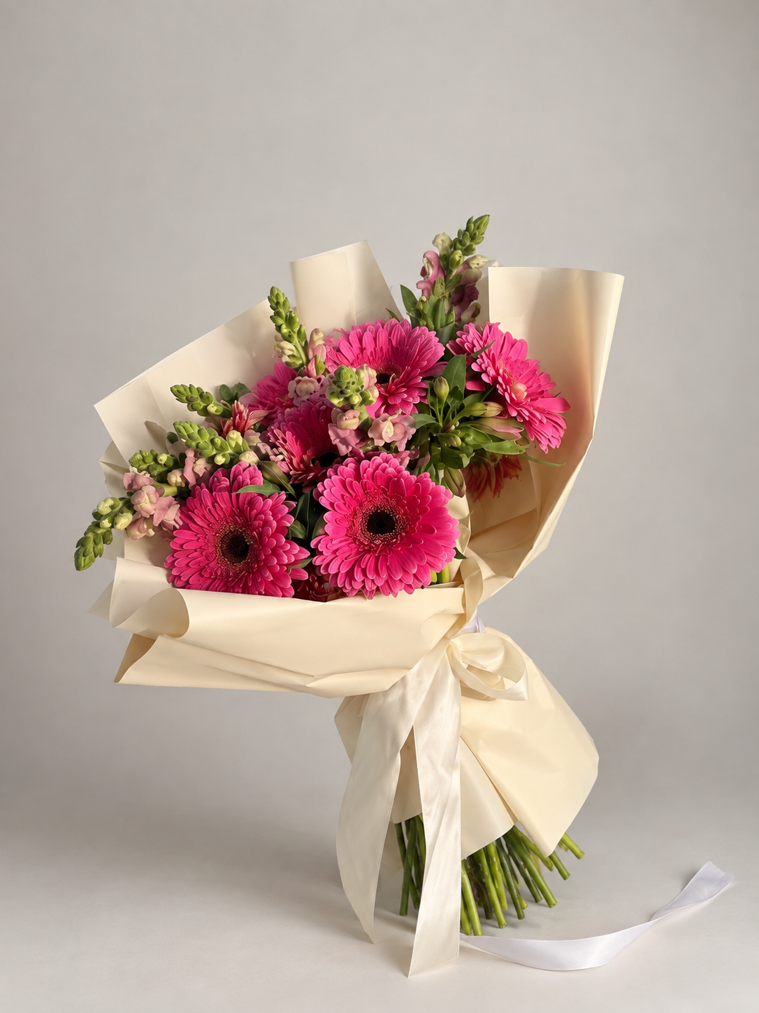 Ramo vibrante de gerberas rosas con flores delicadas y envoltura en tono marfil.