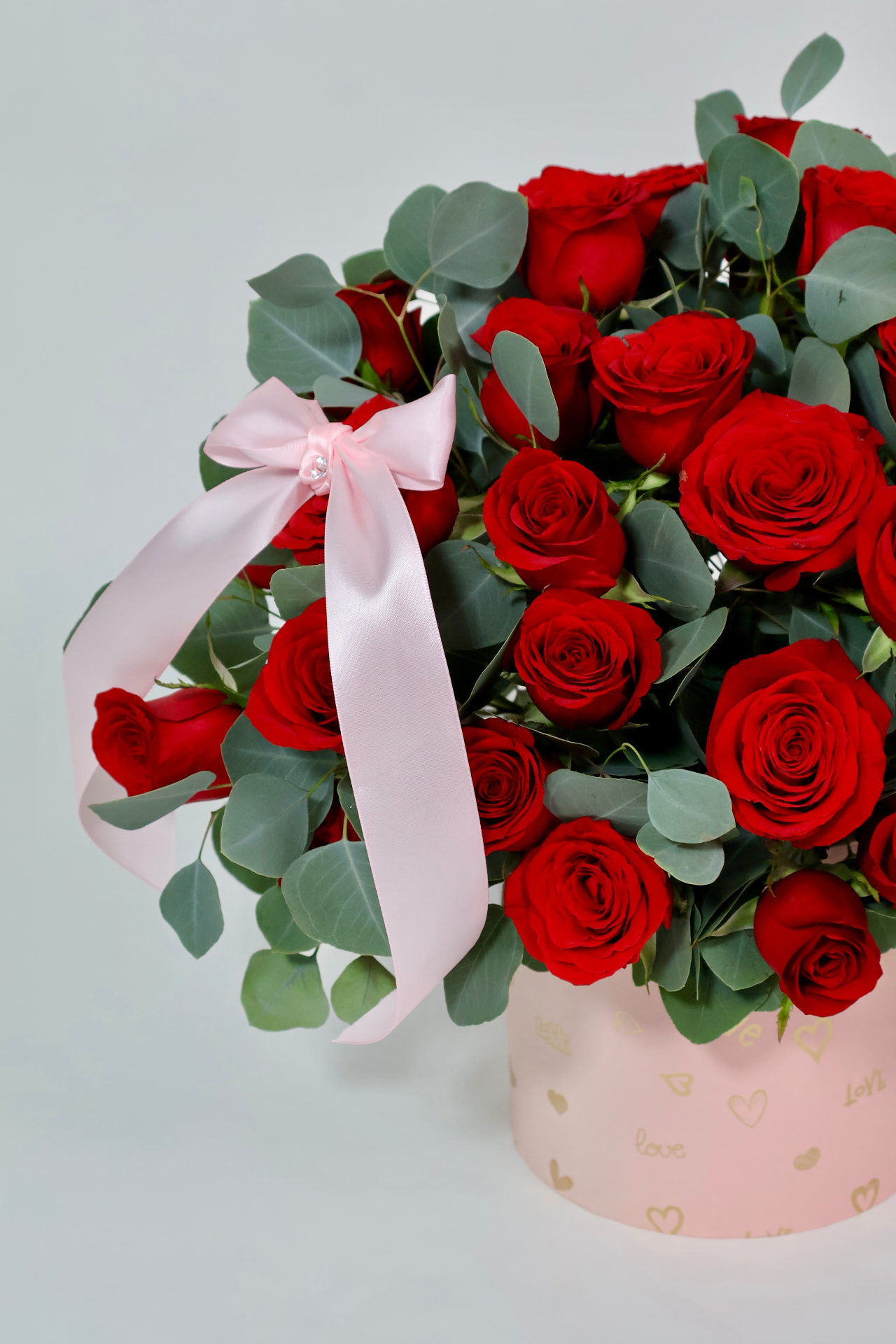 Caja rosa con rosas rojas y eucalipto, terminada con lazo satinado y detalle de corazones.