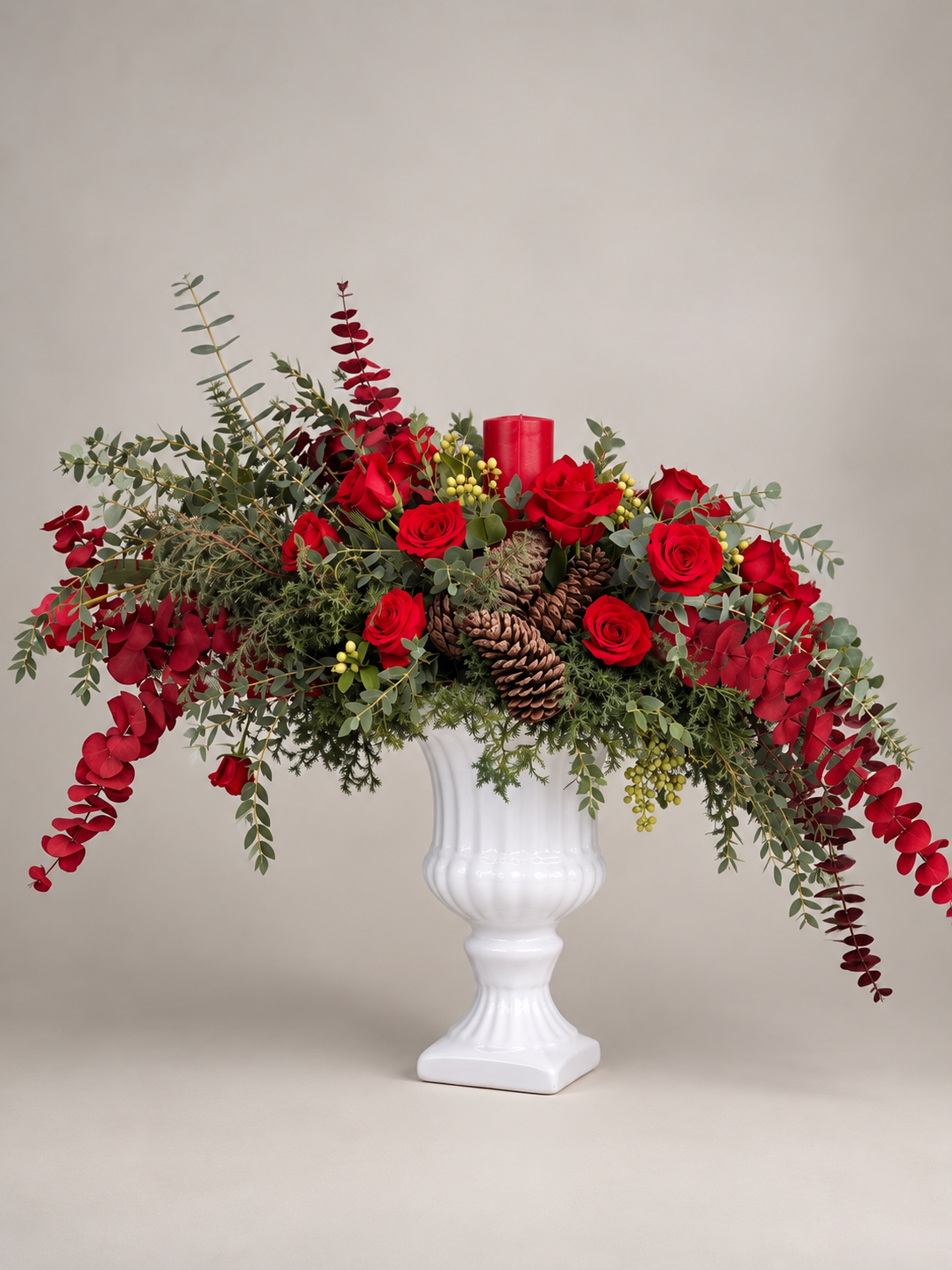 Diseño de temporada con rosas rojas, piñas, follaje abundante y una vela central.