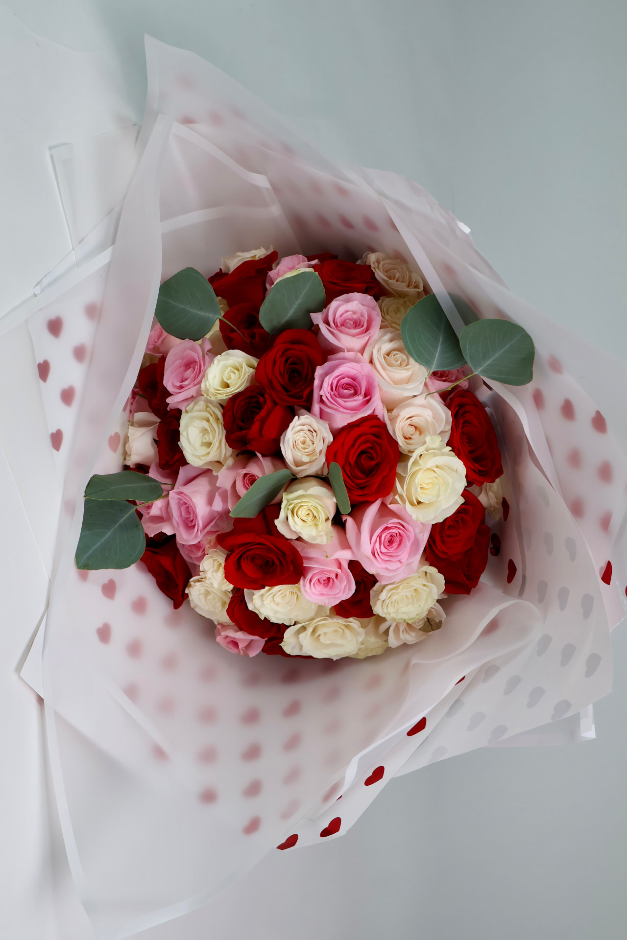 Ramo de rosas rojas, rosadas y blancas con eucalipto, envuelto en papel con detalle de corazones.